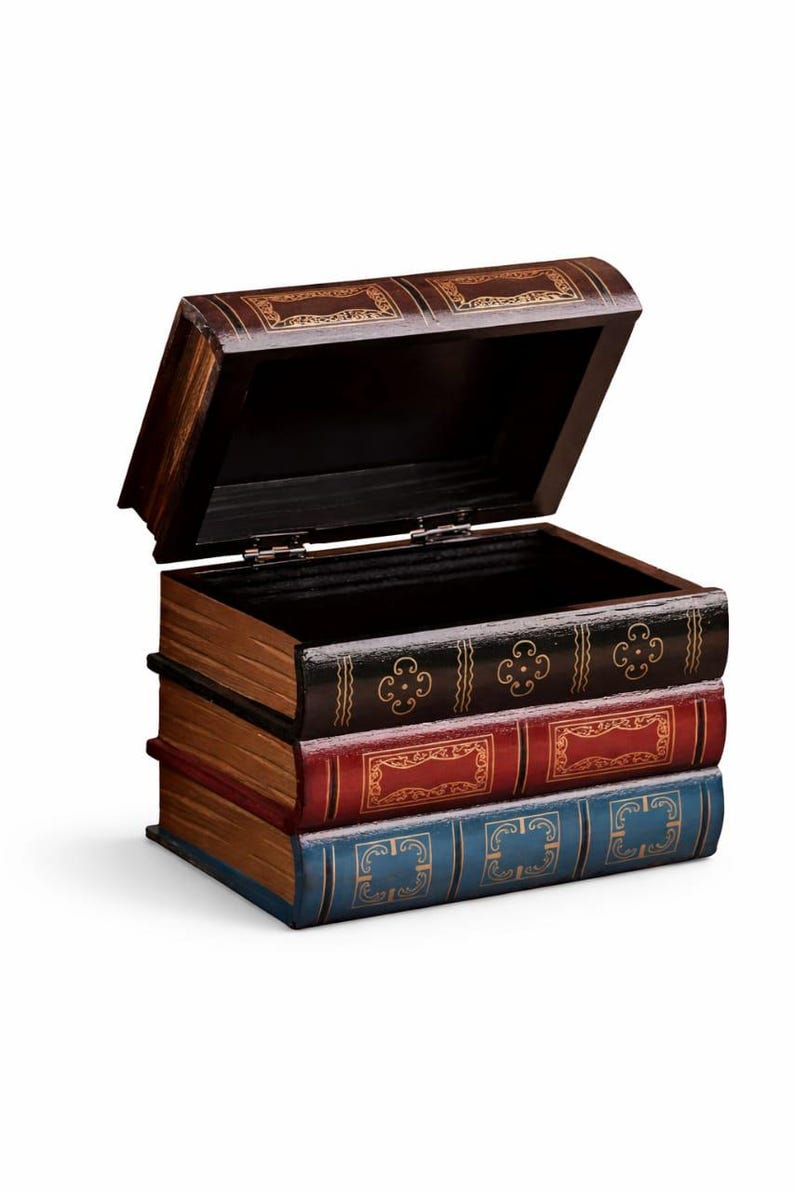 May include: A decorative wooden box designed to resemble a stack of books. The box is dark brown with gold accents and opens to reveal a hollow interior. The "books" are painted in shades of brown, red, and blue.