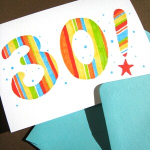 May include: A white card with the number 30 written in colorful stripes. The number 30 is in large, bold font. The card is on top of a blue envelope.