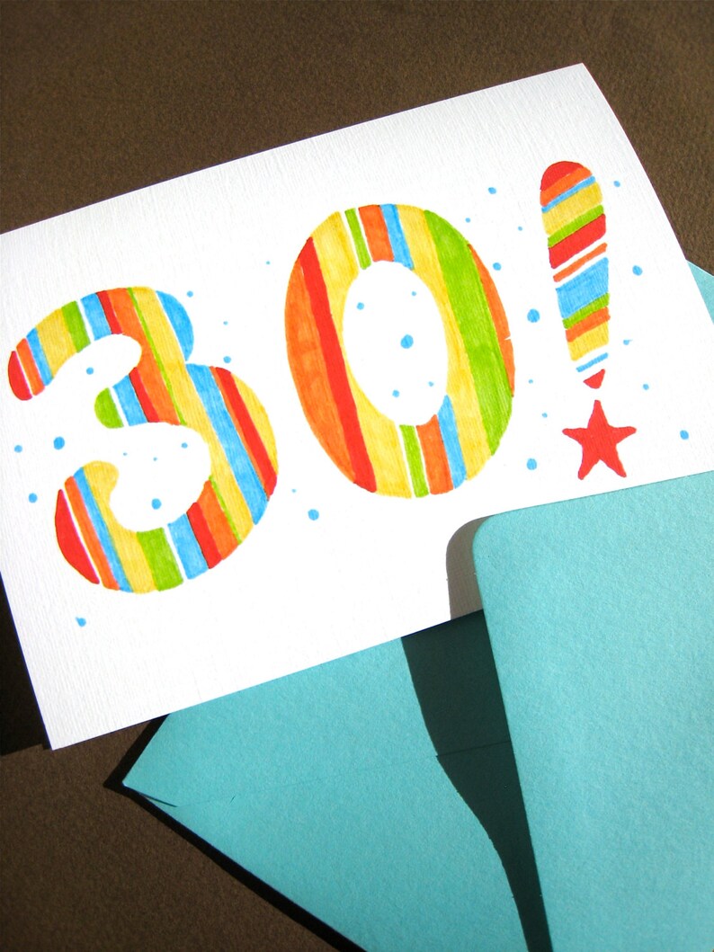 May include: A white card with the number 30 written in colorful stripes. The number 30 is in large, bold font. The card is on top of a blue envelope.