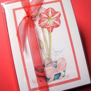 May include: A white card with a red border and a red ribbon tied around it. The card features a watercolor illustration of a red amaryllis flower in a pot with a pink bow. The text "Peace on Earth" is written on a small tag attached to the flower.