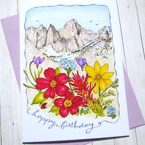 May include: A birthday card with a watercolor illustration of a mountain range with wildflowers in the foreground. The card reads "happy birthday".