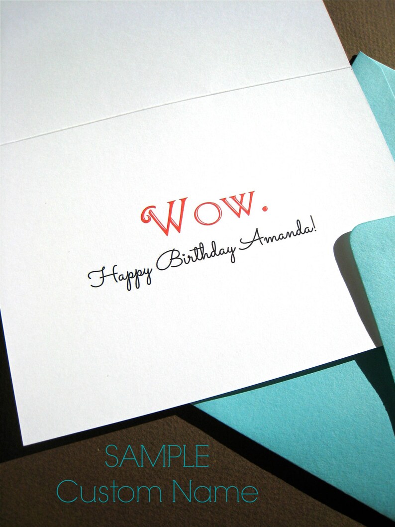 May include: A white card with the text "WOW." in red and "Happy Birthday Amanda!" in black script. The card is folded in half and a light blue envelope is partially visible in the bottom right corner. The text "SAMPLE Custom Name" is printed in black on the bottom of the card.