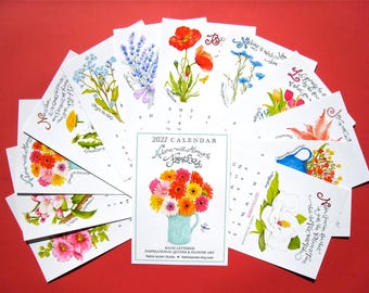 May include: A 2027 calendar featuring hand-lettered inspirational quotes and watercolor flower illustrations. The cover displays a bouquet of colorful gerbera daisies in a light blue pitcher, with individual pages fanned out showing various floral designs.