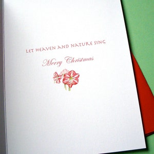 May include: A white card with red text that reads "Let heaven and nature sing Merry Christmas". A small cluster of pink flowers is in the bottom center of the card.