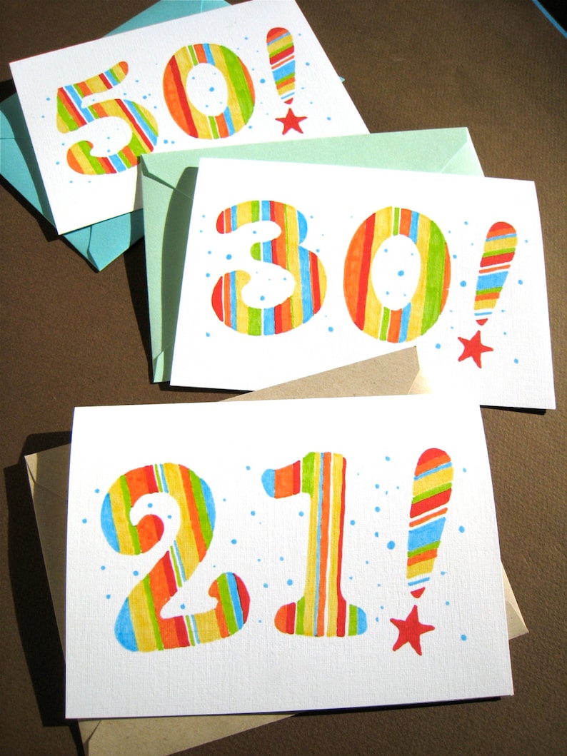 May include: Three white cards with colorful striped numbers and exclamation points. The numbers are 50, 30, and 21. The cards are on a brown surface.