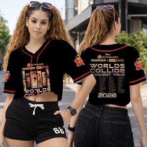 May include: Black baseball-style crop top with red trim, featuring the text "Descendants Zombies + Camp Rock Worlds Collide Concert Tour 2026." The front displays character images. The sleeves have red and white accents.