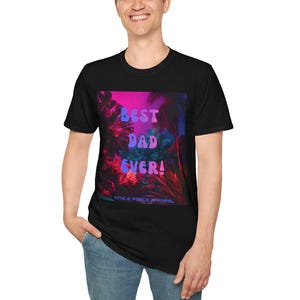 K&ouml;nnte beinhalten: Ein schwarzes T-Shirt mit kurzen &Auml;rmeln und einem rechteckigen Grafikdruck auf der Brust. Das Motiv zeigt eine lebendige tropische Dschungelszene in Pink-, Lila- und Blaut&ouml;nen mit dem Text BEST DAD EVER! und STYLE FORCE APPAREL.