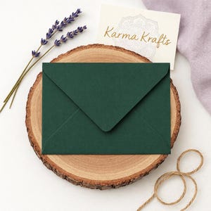 May include: A dark green envelope on a wooden slice, with lavender sprigs and a card reading "Karma Krafts". The envelope is the focal point, with the lavender and card behind. Twine is in the lower right corner.