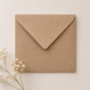 Puede incluir: Un sobre cuadrado hecho de papel kraft texturizado de color marrón claro con una solapa triangular. Una pequeña y delicada rama de flores blancas de paniculata con tallos finos de color verde claro se sitúa cerca de la esquina inferior izquierda.