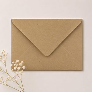 Peut inclure: Une enveloppe rectangulaire en papier kraft brun clair avec un rabat triangulaire. Une petite branche de fleurs blanches de gypsophile avec des tiges vertes fines est placée dans le coin inférieur gauche, chevauchant partiellement l'enveloppe.