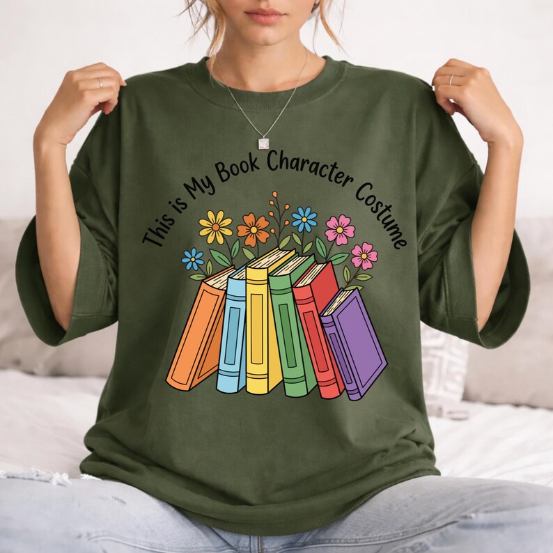 May include: Olive green t-shirt with the text "This is My Book Character Costume" in a curved design. The graphic features a stack of colorful books with flowers above them. The books are orange, blue, yellow, green, red, and purple.