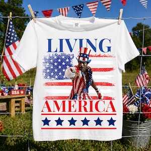 May include: A white short-sleeve t-shirt featuring a graphic of a boxer wearing a red, white, and blue striped top hat and matching outfit. The text "LIVING" and "AMERICA" appears in blue and red, with a row of blue stars at the bottom.
