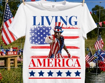 Könnte beinhalten: Ein weißes Kurzarm-T-Shirt mit einer Grafik eines Boxers, der einen rot-weiß-blau gestreiften Zylinder und ein passendes Outfit trägt. Der Text "LIVING" und "AMERICA" erscheint in Blau und Rot, mit einer Reihe blauer Sterne am unteren Rand.