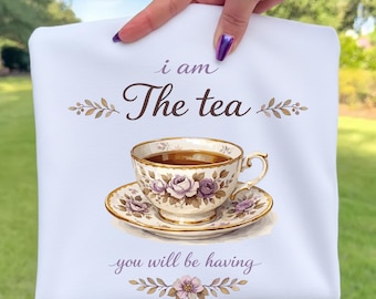 Könnte beinhalten: Weißes Geschirrtuch mit dem Text "i am The tea you will be having" und einer Aquarellillustration einer Teetasse und Untertasse. Die Teetasse ist mit Tee gefüllt und mit lila Rosen und goldenen Verzierungen verziert.