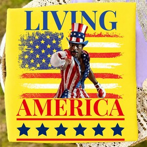 May include: A bright yellow t-shirt featuring the text LIVING AMERICA in blue and red. The graphic shows a person wearing a red, white, and blue top hat and boxing attire, posed in front of a stylised American flag with blue stars at the bottom.