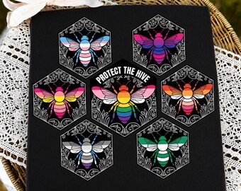 Könnte beinhalten: Eine schwarze quadratische Leinwand mit sechs sechseckigen Rahmen mit weißen floralen Umrissen. Jedes Sechseck enthält eine Biene, deren Flügel und Körper in verschiedenen Pride-Flaggen-Mustern gefärbt sind. Das mittlere Sechseck zeigt den Text PROTECT THE HIVE.