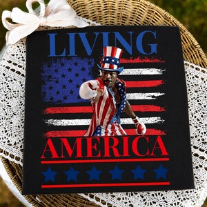 May include: A black square sign featuring the text LIVING AMERICA in blue and red. The centre shows a boxer wearing a red, white, and blue top hat and matching boxing trunks with white gloves, set against a distressed American flag background.