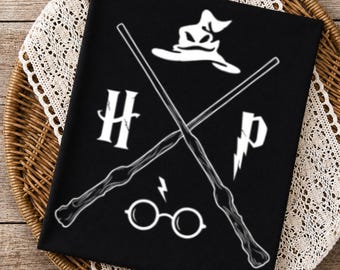 Könnte beinhalten: Ein schwarzes T-Shirt mit einem weißen Grafikdruck von zwei gekreuzten Zauberstäben, einem sprechenden Hut, einer runden Brille mit Blitzsymbol sowie den Buchstaben H und P. Das Motiv ist mittig auf dem Stoff platziert und zeigt magische Symbole.