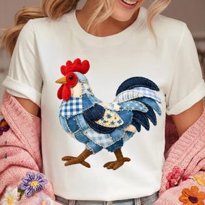 Op de afbeelding: Een wit T-shirt met korte mouwen en een centrale afbeelding van een haan in patchworkstijl. De haan is samengesteld uit diverse blauwe stoftexturen, waaronder ruitjes- en bloemenpatronen, met een felrode kam en lellen.