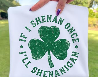 Könnte beinhalten: Weißes Sweatshirt mit einem grünen Kleeblatt und dem Text "IF I * I'LL SHENANIGAN ONCE * SHENANIGAN". Das Design ist in Grün gehalten. Das Sweatshirt wird von einer Hand gehalten.