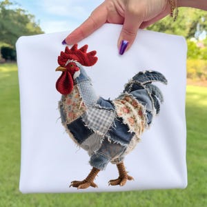 May include: A white square pillow featuring a patchwork rooster design. The rooster has a red comb and wattle, a yellow beak, and a body made of various denim and floral fabric patches. The rooster's legs are brown and textured.
