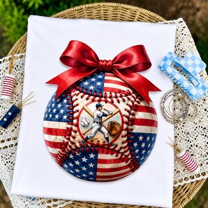 May include: A round baseball-themed ornament featuring a red, white, and blue American flag pattern, topped with a large red satin bow. The centre displays a circular graphic of a baseball player holding a bat, with a baseball and glove nearby.