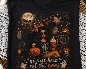 Könnte beinhalten: Ein schwarzes T-Shirt mit einer Grafik einer Person mit Hexenhut und Skelett-Shirt, die einen Kürbiseimer und ein Getränk hält. Das Design zeigt Geister, einen Vollmond, ein Schild mit der Aufschrift TRICK OR TREAT und den Text i'm just here for the boos.