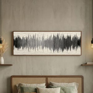 May include: A framed artwork featuring a black and white sound wave design. The artwork is rectangular and mounted on a light-colored textured background. The frame is a dark wood. The artwork hangs above a bed with green and beige bedding.