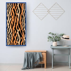 Könnte beinhalten: Ein gerahmtes Wandbild mit blauem Rahmen. Das Kunstwerk zeigt ein auffälliges Muster aus schwarzen und orangefarbenen vertikalen Streifen, das an das Fell eines Tigers erinnert. Das Design ist ein auffälliges Dekorationselement, das jedem Innenraum eine lebendige Note verleiht.