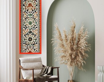 Op de afbeelding: Een lang, rechthoekig kunstwerk met een rode lijst. Het kunstwerk heeft een mozaïekontwerp met geometrische patronen in bruin-, groen- en wittinten. Het kunstwerk hangt boven een houten stoel met een deken.