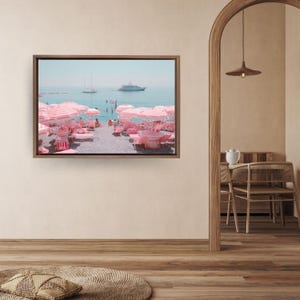 Puede incluir: Impresión enmarcada de una escena de playa con sombrillas y tumbonas a rayas rosas y blancas. Un yate y veleros son visibles en el agua azul. La gente disfruta de la playa bajo las sombrillas.