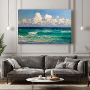 Puede incluir: Una impresión en lienzo rectangular que representa un paisaje marino con un cielo azul brillante lleno de nubes blancas y esponjosas. El océano pasa del turquesa al azul profundo, con olas visibles. La obra de arte se exhibe sobre un sofá gris.