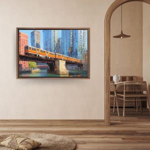 Peut inclure: Peinture encadrée représentant un train orange sur un pont au-dessus d'une rivière. Le paysage urbain comprend de grands immeubles aux façades bleues et blanches. L'œuvre est dans un cadre en bois.