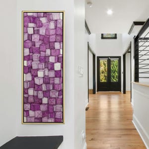 May include: Abstract artwork in a gold frame, depicting a 3D cube pattern in shades of purple and white. The rectangular canvas is mounted on a white wall in a hallway with wooden flooring. The artwork adds a modern touch.