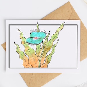 May include: Greeting card with a watercolour illustration of a Venus flytrap plant. The plant has teal traps with a pink centre, set against green and orange foliage. The card is on a white background, with a brown envelope.