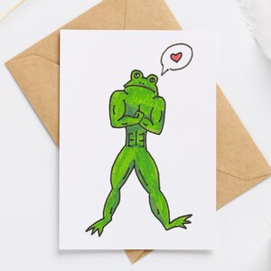 May include: A greeting card featuring a green frog with a muscular physique, arms crossed, and a thought bubble with a heart. The card is on a white background, with a brown envelope behind it.