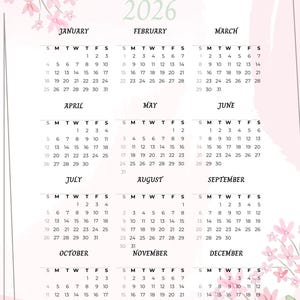 Op de afbeelding: Een kalender voor 2026 met een zachtroze en groene bloemenontwerp. De kalender toont de maanden januari tot en met december, met de dagen en data van elke maand duidelijk zichtbaar. Het woord "Kalender" en het jaar "2026" staan bovenaan.