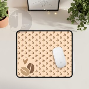 May include: A rectangular mouse mat with a coffee-themed design. The mat has a beige background with a repeating pattern of coffee beans and hearts. Two large coffee beans and hearts are on the left. A white computer mouse rests on the mat.