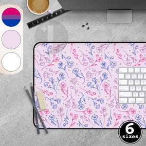 Peut inclure: Tapis de bureau rectangulaire avec un motif floral rose, bleu et rouge. Le tapis a une bordure noire et un clavier blanc sur le côté droit. L'image montre également une tasse de café, des crayons et une gomme.