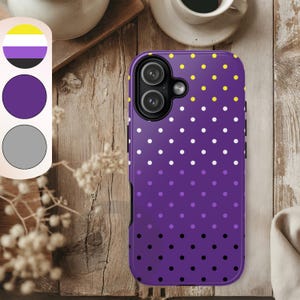 Puede incluir: Una funda de teléfono morada con un patrón de lunares, que transiciona de amarillo a blanco, a morado y a negro. La funda presenta un recorte para la cámara y una paleta de colores de la bandera del orgullo no binario.