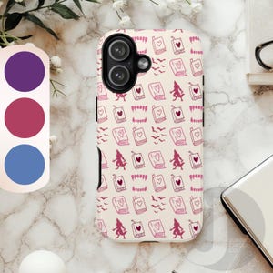 May include: A phone case with a repeating pattern of pink illustrations of books with hearts, bats, and figures on a cream background. The case has a black camera cutout and a color palette of purple, pink, and blue.