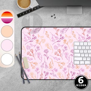 Peut inclure: Un tapis de souris rose à motifs floraux avec un clavier blanc, des crayons et une gomme. Le tapis de souris présente un motif répétitif de fleurs roses, oranges et violettes. L'image montre également une palette de couleurs et le texte "6 tailles".
