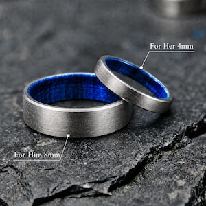 May include: Two rings with a brushed silver-tone exterior and a vibrant blue interior. The larger ring is labeled with the text For Him 8mm, and the smaller ring is labeled with the text For Her 4mm, indicating their respective widths in millimeters.