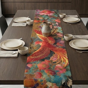Puede incluir: Una mesa de comedor de madera oscura con un colorido camino de mesa con un diseño de fénix y motivos florales en rojo, naranja y azul. La mesa está puesta con platos, cuencos y cubiertos. La mesa está rodeada de sillas.