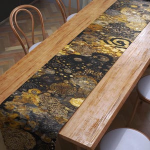 Puede incluir: Una mesa de comedor rectangular de madera con un camino de mesa decorativo con un diseño dorado y negro. La mesa está rodeada por ocho sillas de madera con asientos blancos. La habitación tiene suelo de parquet.