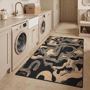 May include: A laundry room with beige cabinets, a white sink, and two washing machines. A black and tan patterned rug covers the floor. The room has a neutral color palette with gold hardware and lighting.