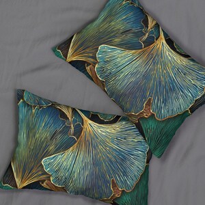May include: Two rectangular throw pillows with a botanical design. The pillows feature a pattern of stylized ginkgo leaves in blue, teal, and gold. The pillows are placed on a grey surface.