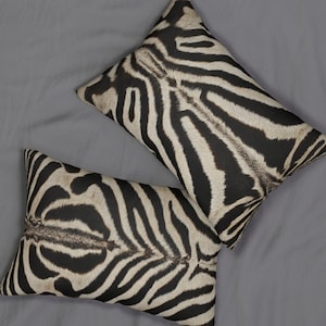 May include: Two rectangular cushions with a zebra print design. The cushions have black and white stripes, with a natural texture. They are arranged on a grey surface.