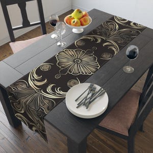 May include: A dark brown table runner with a floral design in beige and cream tones. The runner is placed on a dark wooden table set for a meal, with plates, silverware, and wine glasses.