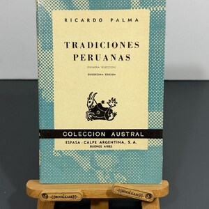 May include: A book titled Tradiciones Peruanas by Ricardo Palma, featuring a light blue cover with a white halftone pattern, a cream-colored center panel, a black goat illustration, and the text Coleccion Austral, Espasa-Calpe Argentina, S.A.